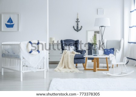 Marine style child's bedroom with lifebuoy on crib, anchor and white rocking horse near armchairs and table