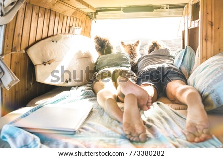 Hipster couple with cute dog traveling together on vintage van transport - Life inspiration concept with hippie people on minivan adventure trip watching sunset in relax moment - Warm sunshine filter Royalty-Free Stock Photo #773380282