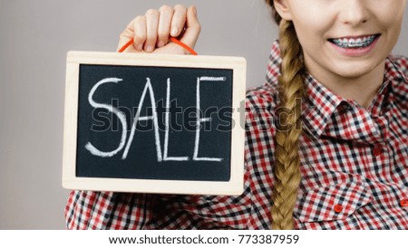 Unrecognizable woman wearing checked shirt holding sign banner with sale on black board.