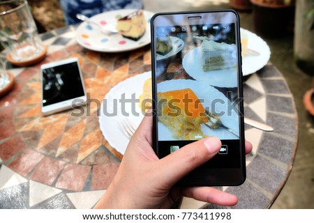 Woman's hand taking photo of sweet orange cake on mobile phone while sitting in cafe , female looking and using cellphone during breaking and relaxing time 