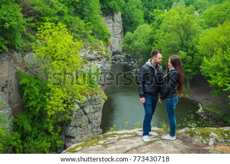 two peolple standing at the edge of a cliff, holding each other, couple in love, a love story on the historical place, casual weared, river and rocks on the background, spring