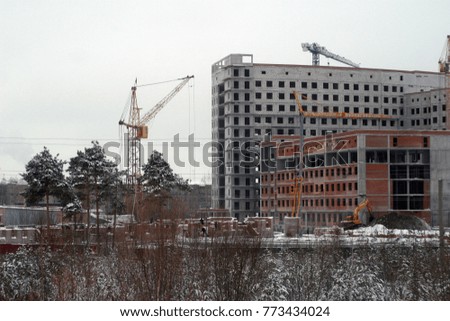 Construction on a snowy white mountain, green pines, a crane, a building under construction. Winter industrial background