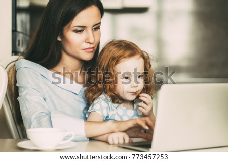 Serious young mother using laptop with daughter