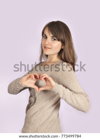 a pretty teenage girl shows heart hand sign isolated on pink background