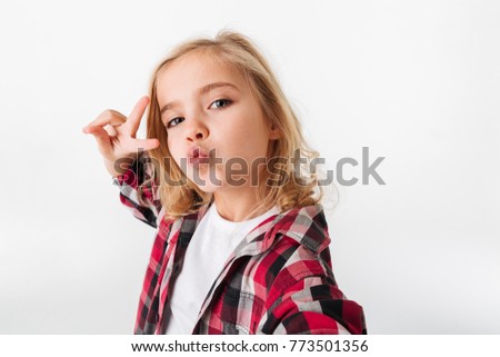 Portrait of a funny little girl grimacing while taking a selfie isolated over white background
