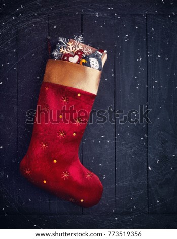 Red stocking with presents and toys on dark wooden textured background with snowfall on Christmas