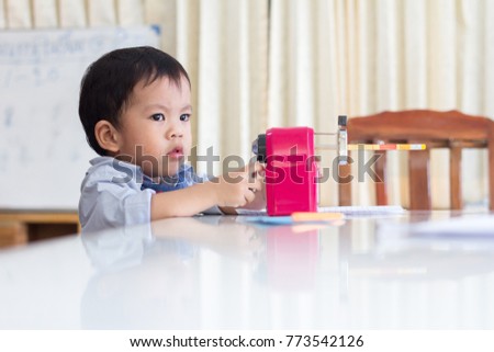 The Adorable little asian boy at the table trying to sharpens the a pencil on bookcase background at the library.Educational Learning Concept.