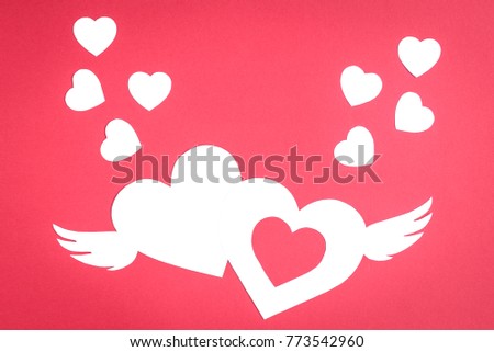 Two white paper hearts  with wings and small white hearts on red background with copy space. Valentine's day concept.