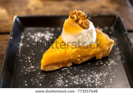 Lemon mousse pie with cream and nuts in black plate on wooden table background.