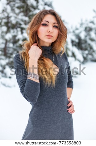 Beautiful young girl posing in the winter in cold forest with pine trees.