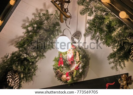 Beautiful Christmas decorations hanging on doors outside the house. Green needle crown with pine cones, angels, dry fruits, elf and red ribbons. Bright Christmas lights around.