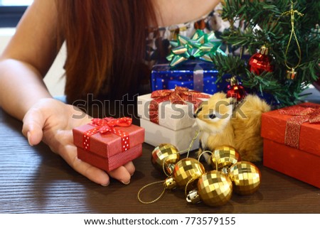 Red gift box hold on women 's hand near Christmas tree.