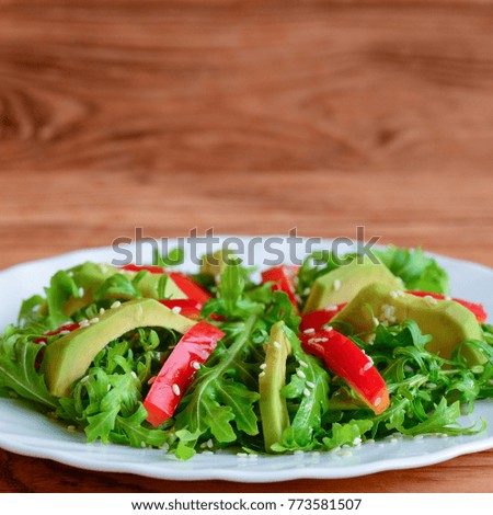 Home healthy salad for lunch or dinner. Raw avocado, arugula, red pepper and sesame seeds salad on a white plate. Raw vegan meal. Closeup
