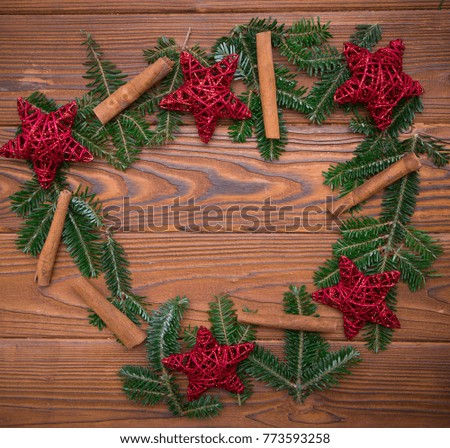 A cute Christmas wreath made of natural fir tree branches, red stars, and cinnamon sticks on a rustic wooden table. Christmas or New Year background. Space for your text or product display. Top view.