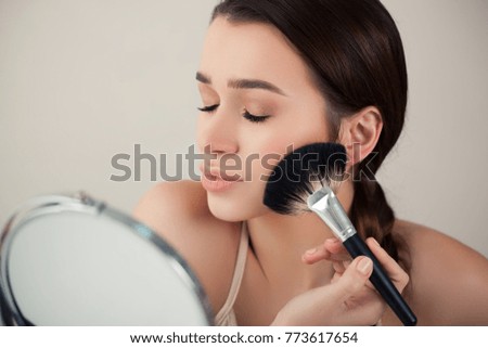 Beautiful Photo girl, woman in the mirror puts makeup brush for publication in magazine or advertisement