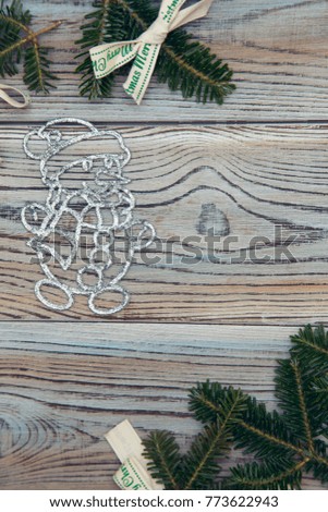Light wooden shabby background for Christmas or New Year with a frame of spruce branches and white textile bows with Merry Christmas inscription and a silver snowman. Top view.