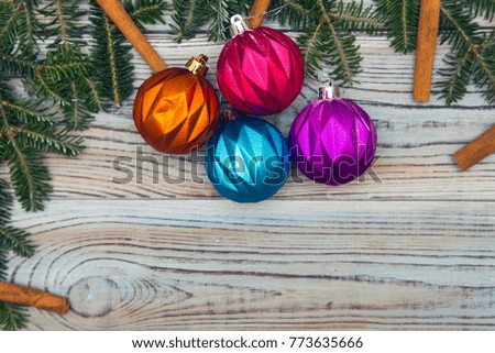 Light wooden shabby background with a frame of spruce branches, cinnamon sticks, and bright Christmas tree balls. Space for your text or product display. Top view. Close up