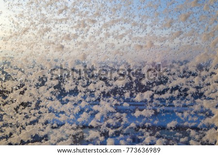 Winter window covered with the first snow. The city landscape which is lit by the morning sun is visible through the window glass.