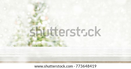 Empty white wooden table top with abstract muted blur christmas tree and snow fall background with bokeh light,Holiday backdrop,Mock up banner for display or montage of product.