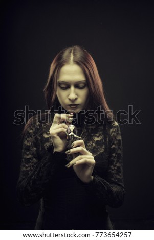 Gothic pale girl holding voodoo doll over black background