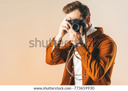 obscured view of fashionable man taking picture on photo camera isolated on beige
