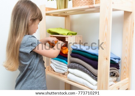 The girl is measuring her mother's clothes and shoes. Order in the closet. Smart storage system. Capsule wardrobe. The girl plays and puts mother's clothes in order or chaos. Wardrobe order. Royalty-Free Stock Photo #773710291