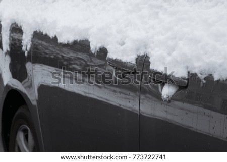SIDE OF A CAR WITH DOOR HANDLE COVERED BY SNOW IN WINTER TIME 