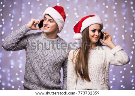 Young couple are speaking their phones wearing santa hat on light bokeh background