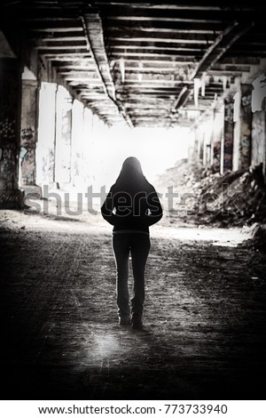 Light at the end of the tunnel.  A  silhouette of a woman walks out of an abandoned subway tunnel walking toward the light. Royalty-Free Stock Photo #773733940