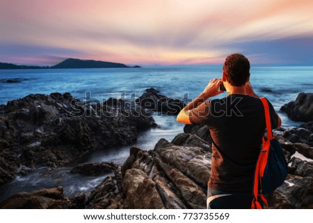 Man using smartphone shooting image on sea sunset or sunrise with colorful of sky and cloud with sunlight in twilight motion blur
