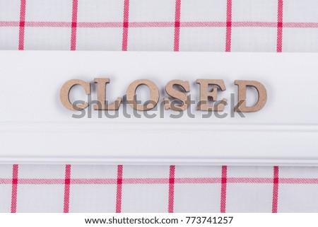 Word closed, abstract wooden letters, background classic tablecloth in a red white cage.