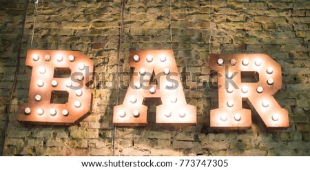 The word "BAR" lights up on a brick wall
