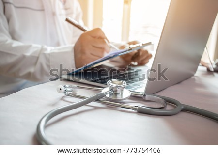 Medicine doctor's writing on laptop in medical office.Focus stethoscope on foreground table in hostpital.Stethoscope is acoustic medical device for auscultation,listening internal sounds of human body Royalty-Free Stock Photo #773754406