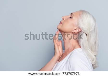 Advertisement concept. Close up profile with copy space of nice, charming, aged woman, touching her skin of neck with hand over grey background Royalty-Free Stock Photo #773757973