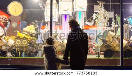Rear of the silhouette of little girl and her father coming close to the shop window and looking at the great Christmas fairy show in the night. Outdoors