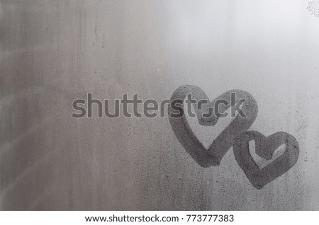 Couple of abstract blurred love heart symbol drawn by hand on the wet window glass with sunlight background. Template for Valentine Day postcards