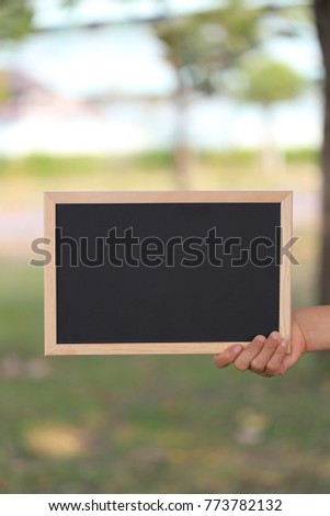 Hand of a business woman holding a empty black wooden picture frame on blur garden background and have copy space to input ideas in your work.