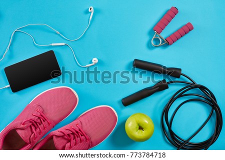 Flat lay shot of sneakers, jumping rope, dumbbells and smartphone on blue background. Royalty-Free Stock Photo #773784718