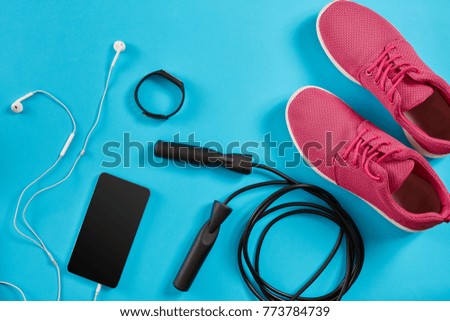 Flat lay shot of Sport equipment. Sneakers, jump rope, earphones and phone on blue background.