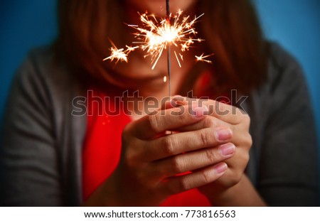 Happy Asian Woman in red shirt having fun with sparkler on blue background.