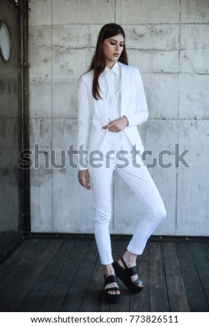 Portrait of young lady with dark hair standing in classic white suit and black shoes isolated