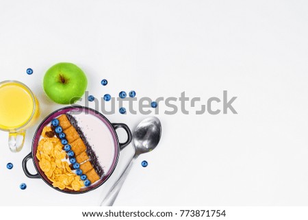 Breakfast, bowl with homemade yogurt and cornflakes, and fresh blueberries, a glass of orange juice, and a green apple on a white background, top view, flat lay. Concept of  healthy food, detox.