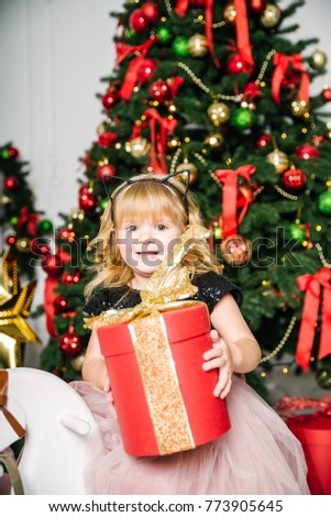 mother with daughter sitting near christmas tree and opening gifts fire place with chair on background