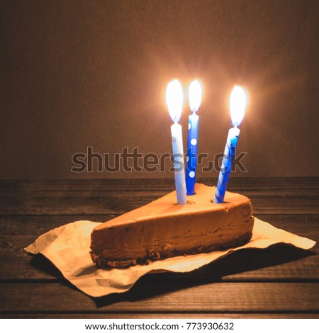Chocolate cheesecake with three  burning blue candles on dark background.