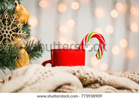 A Christmas tree decorated snowflakes and a garland, cup of coffee, candy with knitted scarf on the background of a bokeh and white boards. Merry Christmas, ideas for postcards for winter holidays