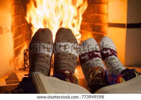 A man and a woman in warm knitted socks with an old book in front of the fireplace. Evening fairy tales. Fantasy.