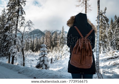 Young female with a bag and hood giving back in a snow forest