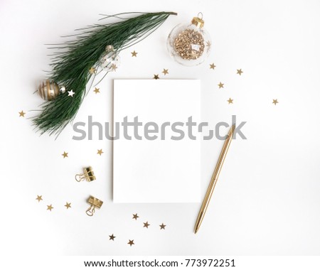 Christmas greeting card template in gold. Empty paper mock up, fir tree branch with glass ball decorations, star confetti, pen on white background. New year flat lay, top view, copy space