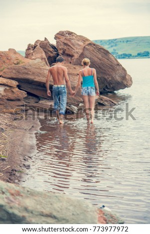 Sea travel, a happy couple is in hand on the sea side near the hot summer waters of the ocean. Honeymoon rocks on the shore.