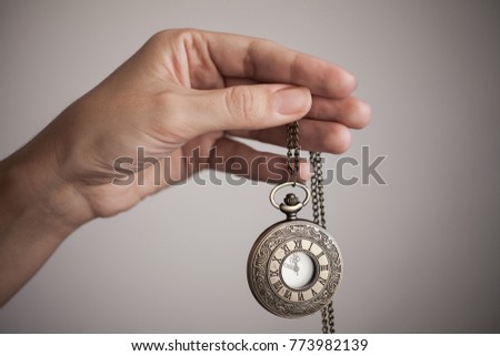 a woman is holding a watch on a chain on a gray background. The time on the clock 11:55 PM